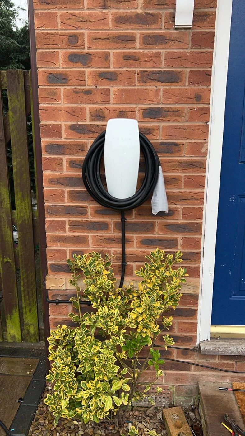 Tesla Wall Connector fitted on a brick wall by the front door of a family home