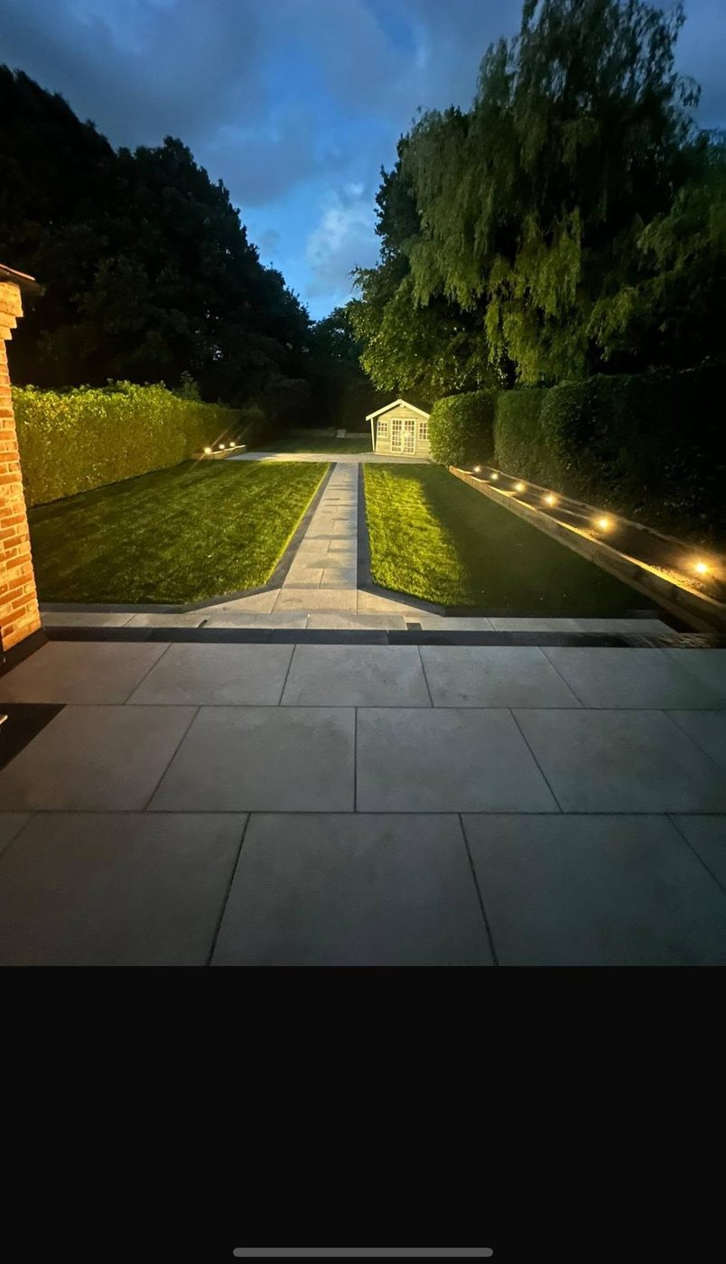 Garden at dusk with warm low-level lighting along the borders and a lit stone path to a summer house