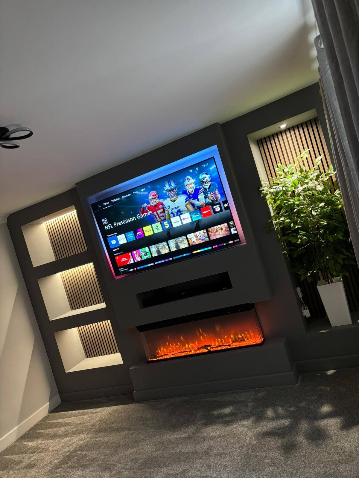 Angled view of a dark media wall showing the recessed TV, soundbar shelf and integrated fire