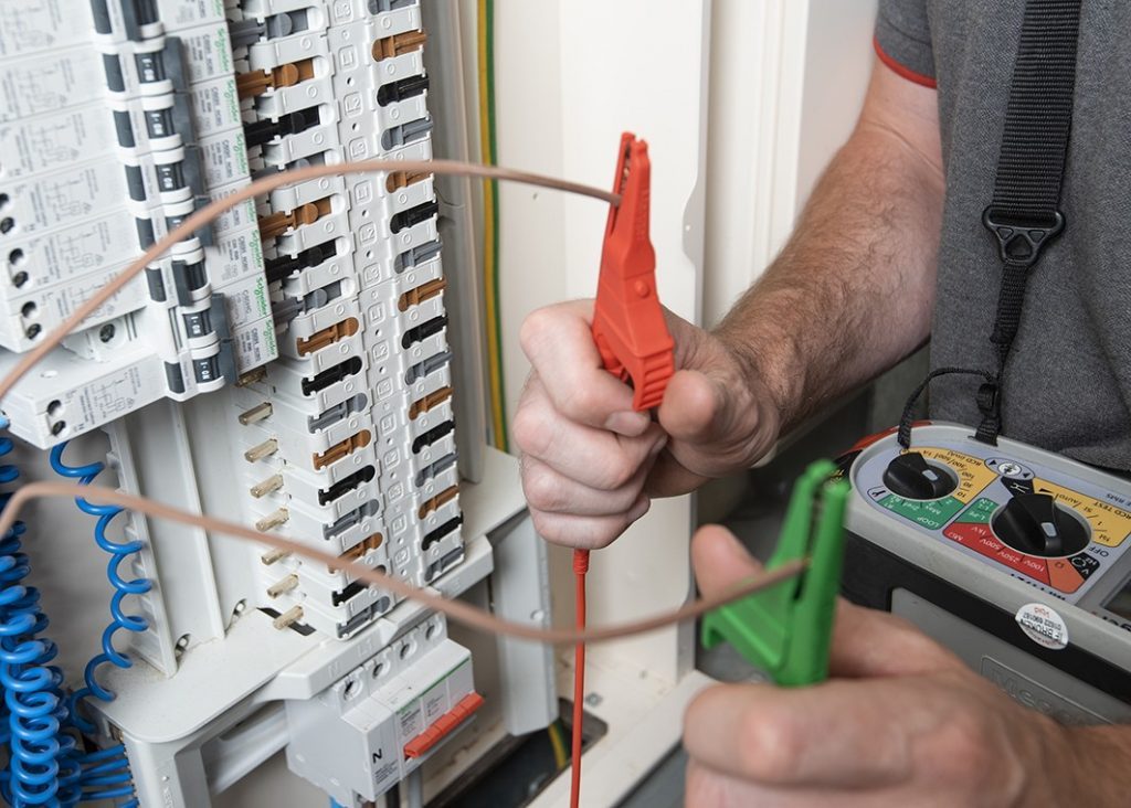 Electrician testing at a consumer unit with red and green test leads while carrying out remedial works