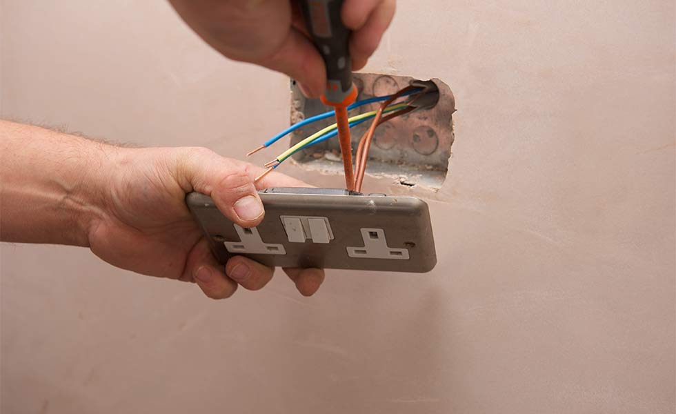 Electrician wiring a new double socket into a back box, the live, neutral and earth conductors exposed